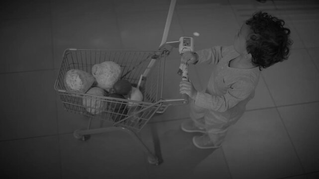Top-down view of child pushing small shopping cart across tiled supermarket floor