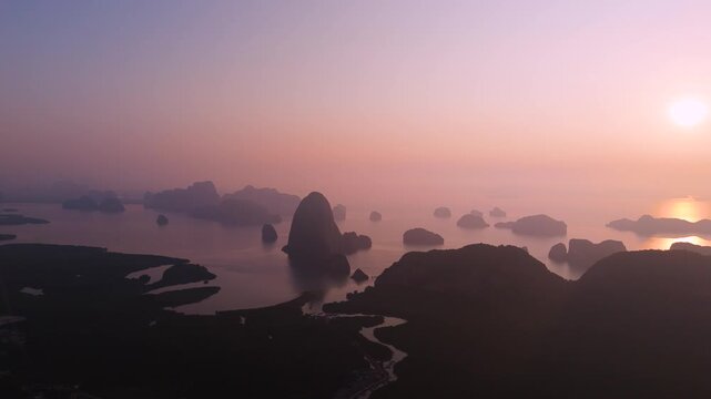 View from above Majestic limestone formations rise above emerald waters fringed by winding mangroves, vibrant coastal village of port is visible against the backdrop of an orange sunrise clouds