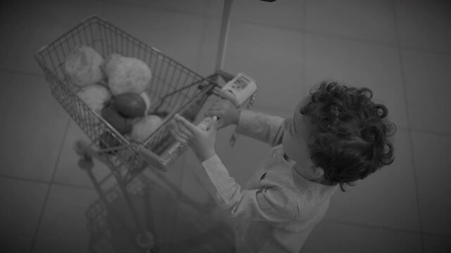 Overhead view of toddler pushing small shopping cart in supermarket aisle