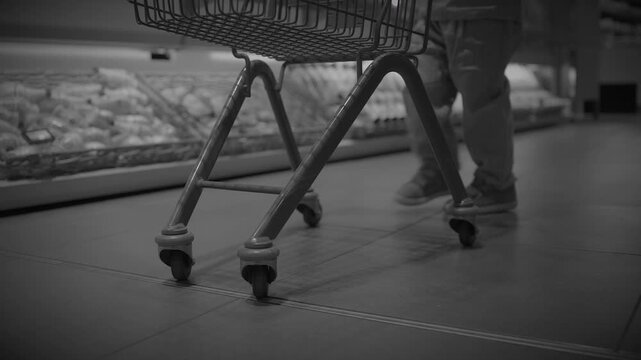 Low-angle close-up of shopper's legs and shopping cart wheel in supermarket aisle