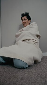Vertical stab shot of middle aged Caucasian woman wearing straitjacket sitting on floor of psychiatric clinic, looking panicked. Footage is ideal for mental health awareness or medical documentaries