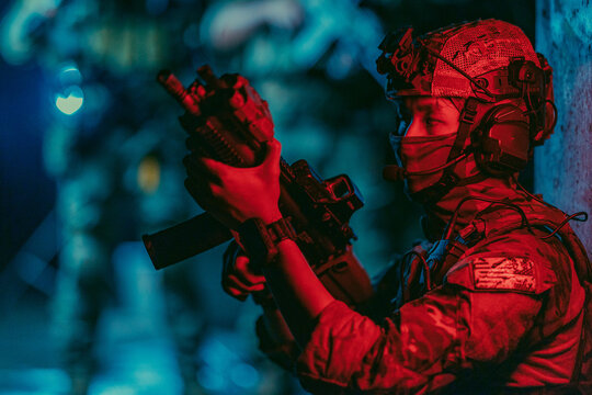 Military tactical team operates under red light at night inside dark abandoned building