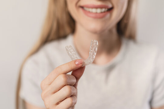 Closeup smiling girl holds transparent silicone night guard to protect teeth from wear. Bruxism. Orthodontic treatment of malocclusion, teeth straightening with aligners.