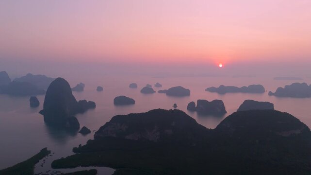 View from above Majestic limestone formations rise above emerald waters fringed by winding mangroves, vibrant coastal village of port is visible against the backdrop of an orange sunrise clouds