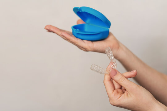 A woman's hands display a transparent night guard for bruxism protection. The guard container is on a white background.