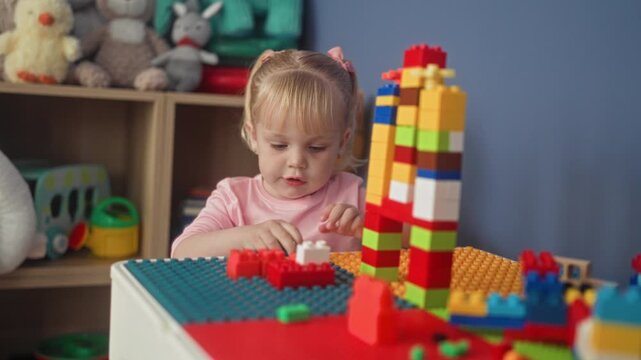Little girl stacking colorful plastic blocks, reaching forward with hand on playtable in building; concentration creativity.