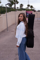 Fototapeta premium Young woman carrying guitar case walking urban park path