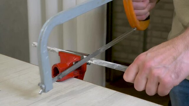 Sawing a board with a hacksaw, a workshop with a clamping vice and a board in a vice.