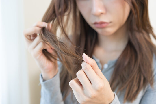Damaged Hair, frustrated asian young woman, girl hand in holding splitting ends, messy unbrushed dry hair with face upset, long disheveled hair, health care of beauty. Portrait isolated on background