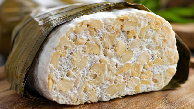 Fresh raw tempeh wrapped in banana leaf on a rustic wooden cutting board