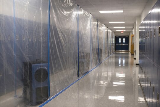 Plastic sheeting containment zone in school hallway featuring an industrial air mover for professional mold remediation and water damage restoration in a public building corridor