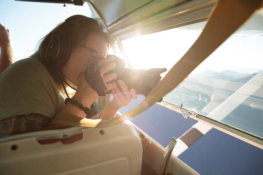 Person using camera inside small plane while flying over landscape
