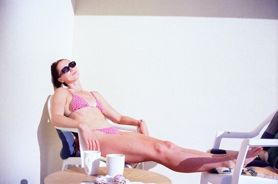 Film photo of a woman sunbathing in a pink swimsuit at a villa.