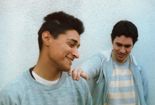 Young man placing hand on friend&rsquo;s shoulder while both smile