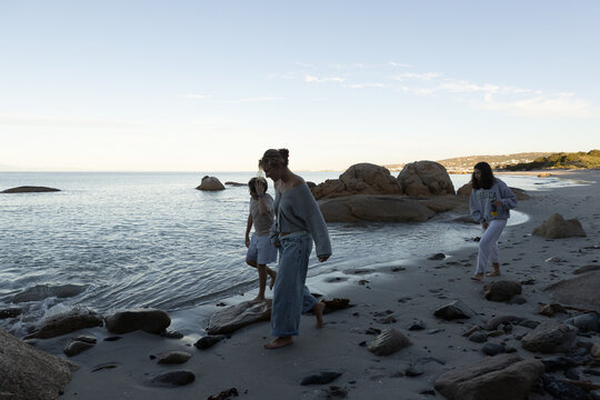desaturated image of siblings walking beach near boulders, Saldanah Bay, Western Cape, South Africa at sunset