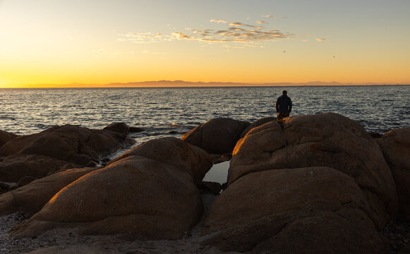 silhouette of man viewing sunrise atop boulder rock, Saldanah Bay, Western Cape, South Africa