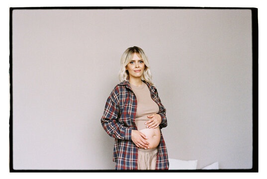 A pregnant woman near a gray wall.