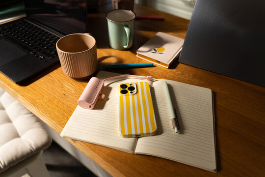 Workspace With Phone, Coffee Mugs, and Notebook on a Wooden Table
