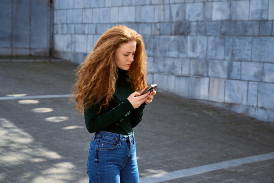 Young Woman Uses Smartphone While Standing Outdoors in Urban Setting