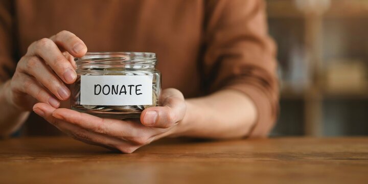 Person holding glass jar filled with coins and label saying donate showing charitable giving concept.