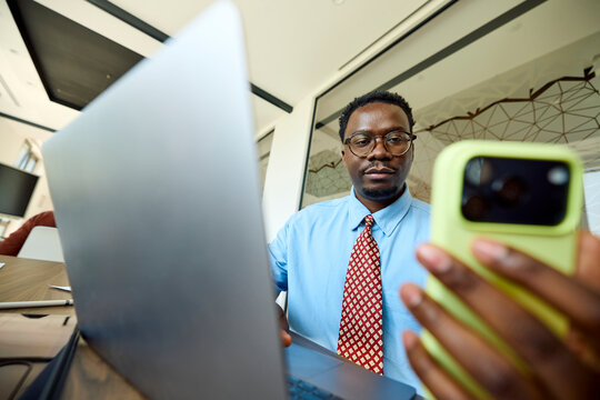 Man sits at the office, using his laptop and a phone