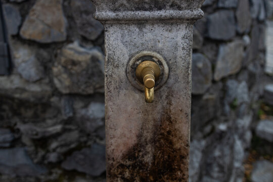 Close-up of a vintage brass faucet with water droplets on a stone public drinking fountain outdoors.