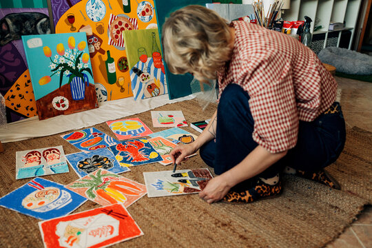 Female artist sitting on floor arranging colorful artworks
