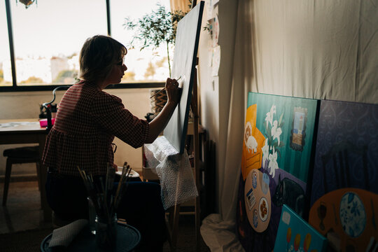 Silhouette of female artist painting at easel near window