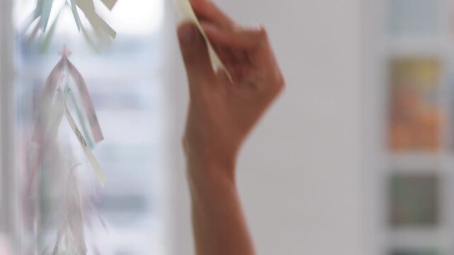 Woman, glass wall and sticky note at office with project management, planning or review at startup. Person, paper and job with solution, proposal or problem solving with schedule at creative agency