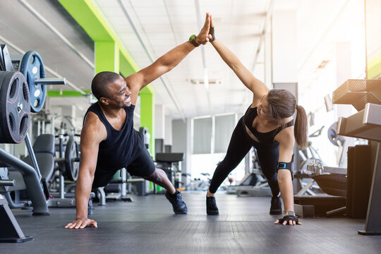 Young Black fitness giving each other a high five while in push-up position on gym floor, both smiling. Energetic partner workout celebration moment in black sportswear in modern gym