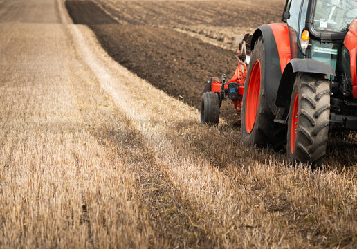 Red tractor plowing agricultural field after harvest, soil cultivation and farm work