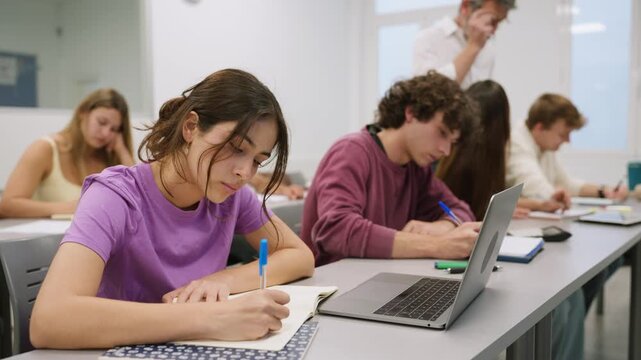 High school students writing in classroom with teacher supervising