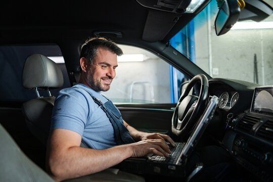 Car mechanic using laptop for diagnostics inside vehicle in auto repair shop