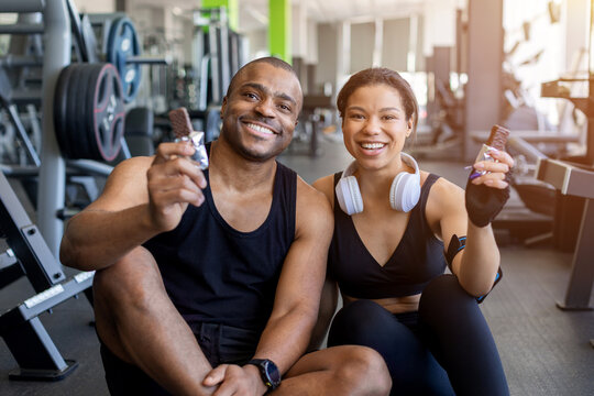 Young black holding protein snack bars after exercise in modern gym. Fitness nutrition, healthy recovery, active lifestyle, and wellness concept