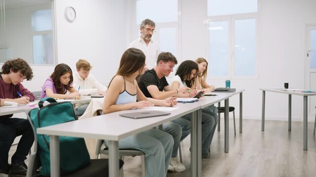 Teacher walking behind students during exam in bright modern classroom