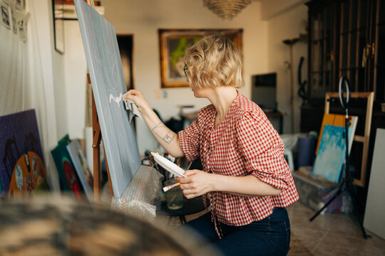 Female artist wiping canvas while adjusting painting in studio