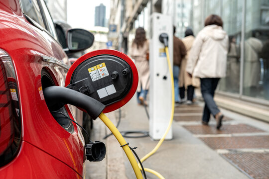 Electric Car Charging at Urban Street Charging Station With Pedestrians and City Buildings