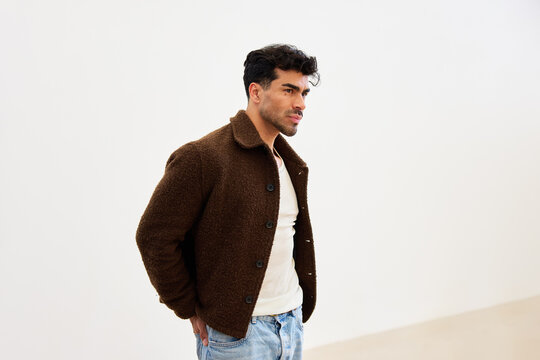 Man in brown jacket stands indoors and looks to the side