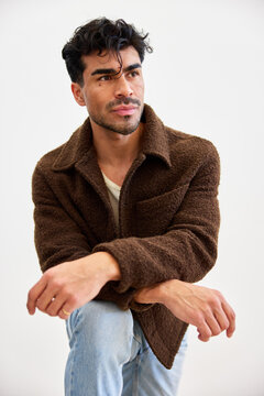 Man in brown jacket poses on one knee in a studio setting