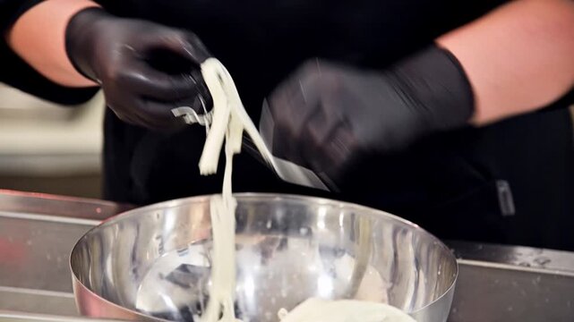 Chef prepares stracciatella cheese by stretching curds in stainless steel bowl
