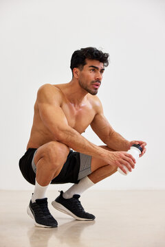 Man does squat exercise while holding a drink in gym