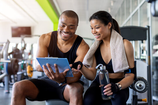 Smiling trainer and client reviewing workout information together in modern fitness center, highlighting progress tracking, motivation and successful fitness coaching