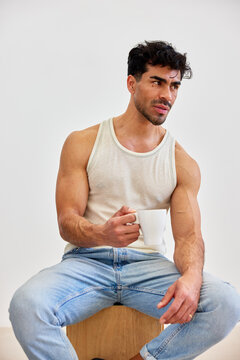 Man sitting on stool holding white cup in bright indoor space