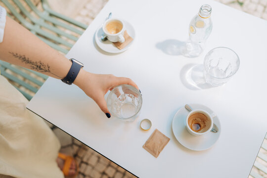 Overhead view of hand reaching for water glass beside espresso
