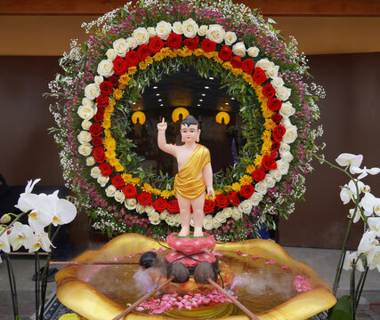 Baby Buddha statue in lotus basin during Vesak ceremony surrounded by floral wreath