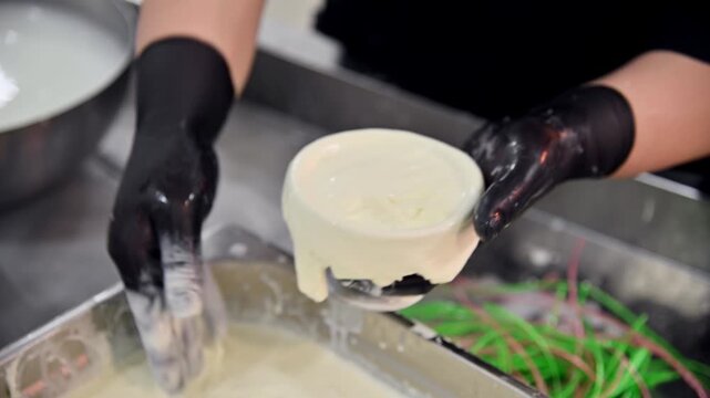 Hands shaping fresh burrata cheese in a kitchen, with bowls and ingredients visible