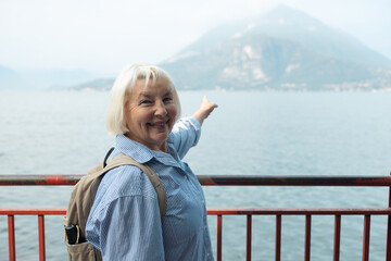 Fototapeta premium Portrait of a happy senior lady with grey hair showing beautiful landscape background on a sunny day during her retirement journey.