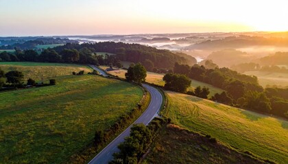 Fototapeta premium Scenic country road winding through rolling hills at sunrise, misty valley.