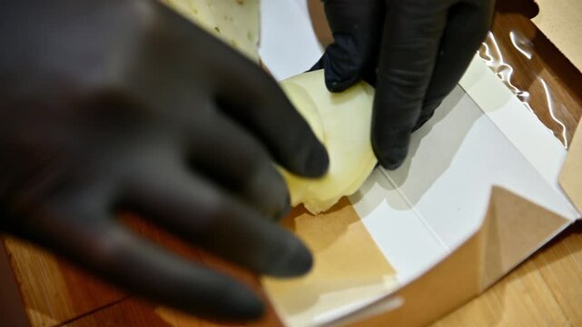 Hands slicing cheese and arranging pieces in a cardboard container for presentation