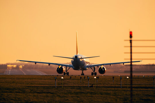 Rear view of passenger airplane taxiing on airport runway for take off during golden sunset dusk. Aviation industry, commercial flight, international travel and transport concept with copy space.